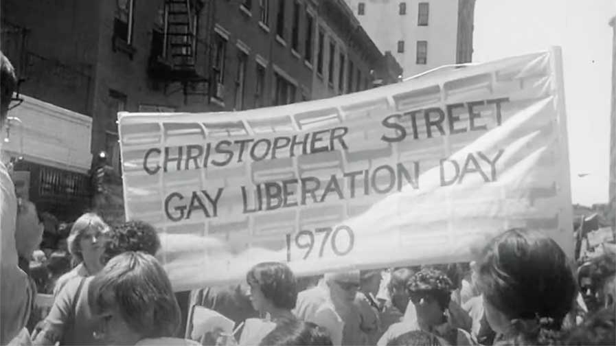 A huge banner reading Christopher Street Gay Liberation Day 1970 is held aloft among a group of people about to set off on the march