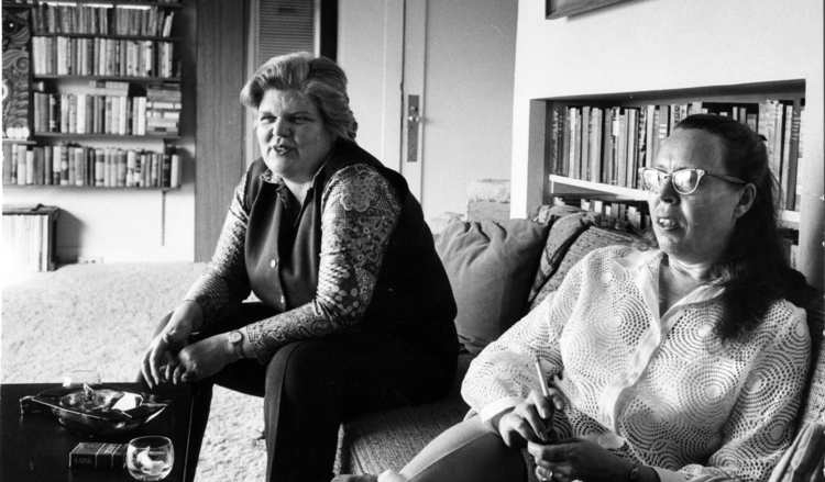 A black and white image showing Del Martin and Phyllis Lyon sitting on a sofa in their in their house in San Francisco in the 1980s